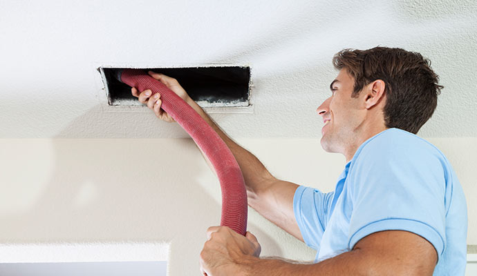 A man cleaning an air duct in the ceiling with a large hose.