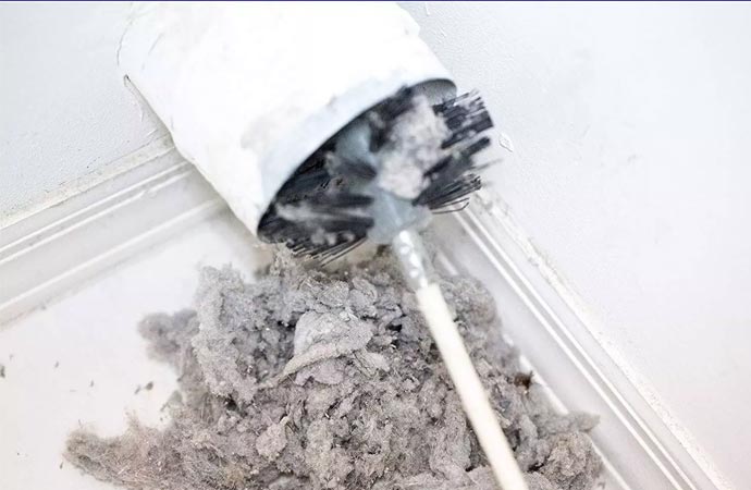 A brush tool is being used to clean out a dryer vent, removing a significant amount of lint and debris.