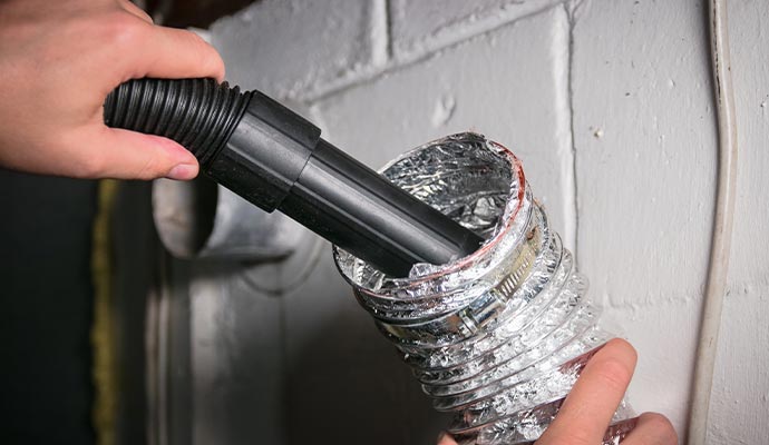 A person cleaning a dryer vent with a vacuum attachment.