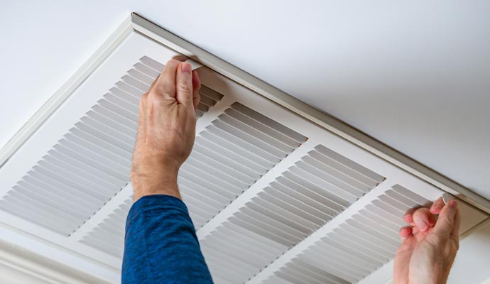 Person removing an air filter from a ceiling vent.