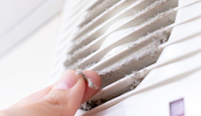 Close-up of a hand pulling dust from a dirty air conditioning vent.
