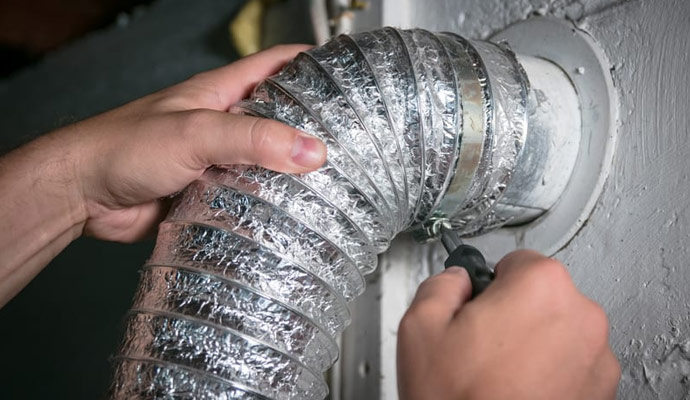 Hands tightening a clamp on a flexible air duct connected to a wall vent.